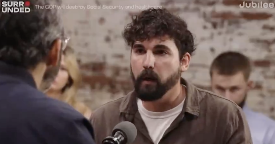 Man in casual shirt speaking into a microphone during a discussion event