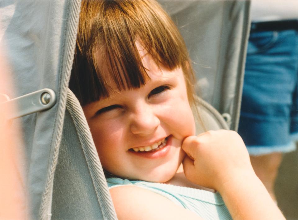 Child smiling while sitting in a stroller, wearing a striped top, with a hand resting on the cheek